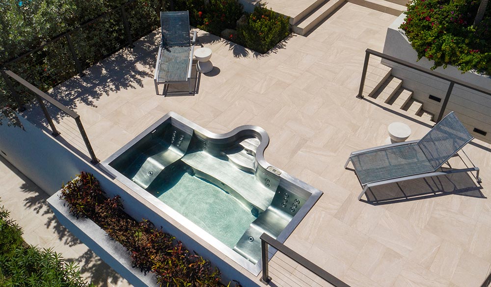 Custom stainless steel rooftop spa with LED lighting, two loungers, bench seating and interior descending stairway. 
