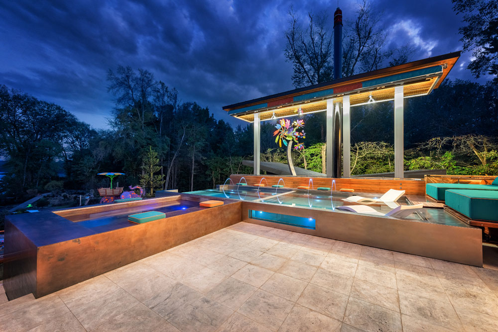 Custom stainless steel pool with sun shelf, descending stairway, bench seating and laminar jets. Glass windows separates pool and neighboring stainless steel and copper spas with vanishing front edge. 
